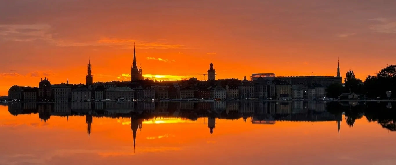 Gamla stan i siluett mot en orange solnedgång som speglas i vattnet